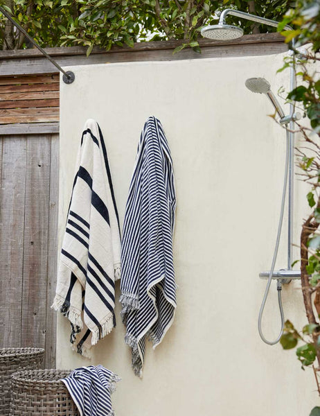 #color::navy-stripe #style::navy-stripe | Navy and white striped Beach Towel by Business & Pleasure Co hangs from an outdoor shower space with another towel