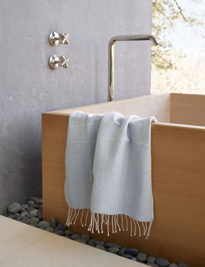 Melkam light gray Hand Towel with fringed ends by Bolé Road Textiles hangs off the side of a rectangular wooden tub