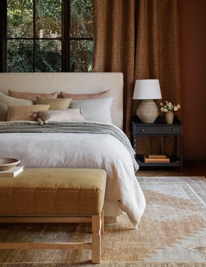 The Ambleside camel linen bench sits atop a patterned rug in a room with accented black wooden walls and a natural linen bed