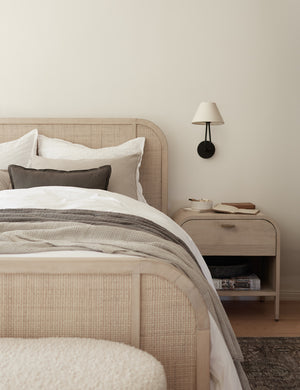 One Hayden double-armed black sconce light hangs on a white wall next to a bed with a white-washed woven frame