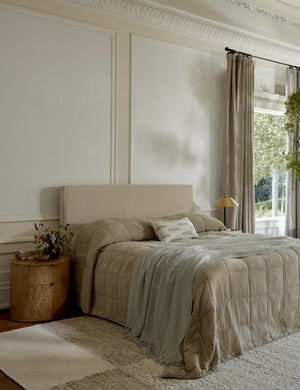 Stripe break natural and cream lumbar pillow by Sarah Sherman Samuel sits on a bed with brown linens in a bedroom with high ceilings