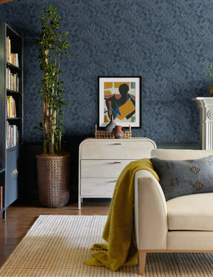 The Bequia Indigo Wallpaper is in a living room with a grid patterned rug, a natural linen sofa, and a whitewashed dresser