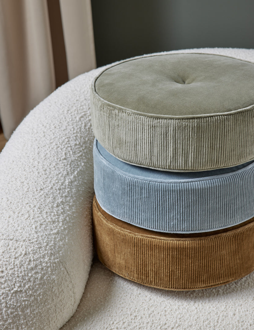 #color::juniper | The Velvet Disc Pillow by Sarah Sherman Samuel in amber, canyon blue, and juniper green are stacked atop each other sitting on a white boucle accent chair