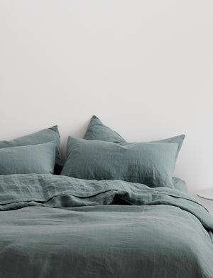 The European Flax Linen blue stone Duvet Cover by Cultiver lays on a bed with other cultiver linens