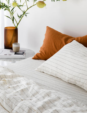 The Set of two european flax linen cedar orange pillowcases by cultiver lay on a bed with pencil stripe linens by cultiver