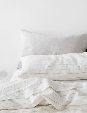 The Set of two european flax linen pencil stripe pillowcases by cultiver lay on a bed with other pencil stripe and smoke gray linens by cultiver