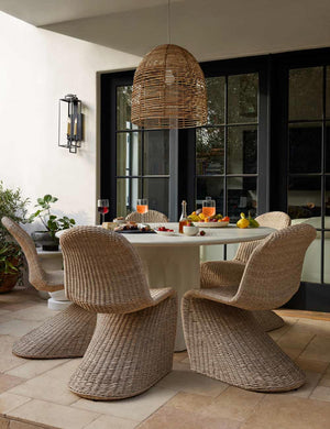 The Beehive jute woven pendant light is hung in a patio over a circular dining table that is surrounded by woven chairs