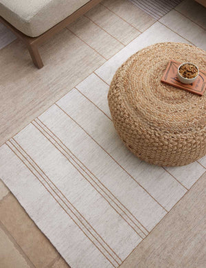 The valencia indoor and outdoor rug lays in an outdoor space under a sectional sofa and a woven ottoman