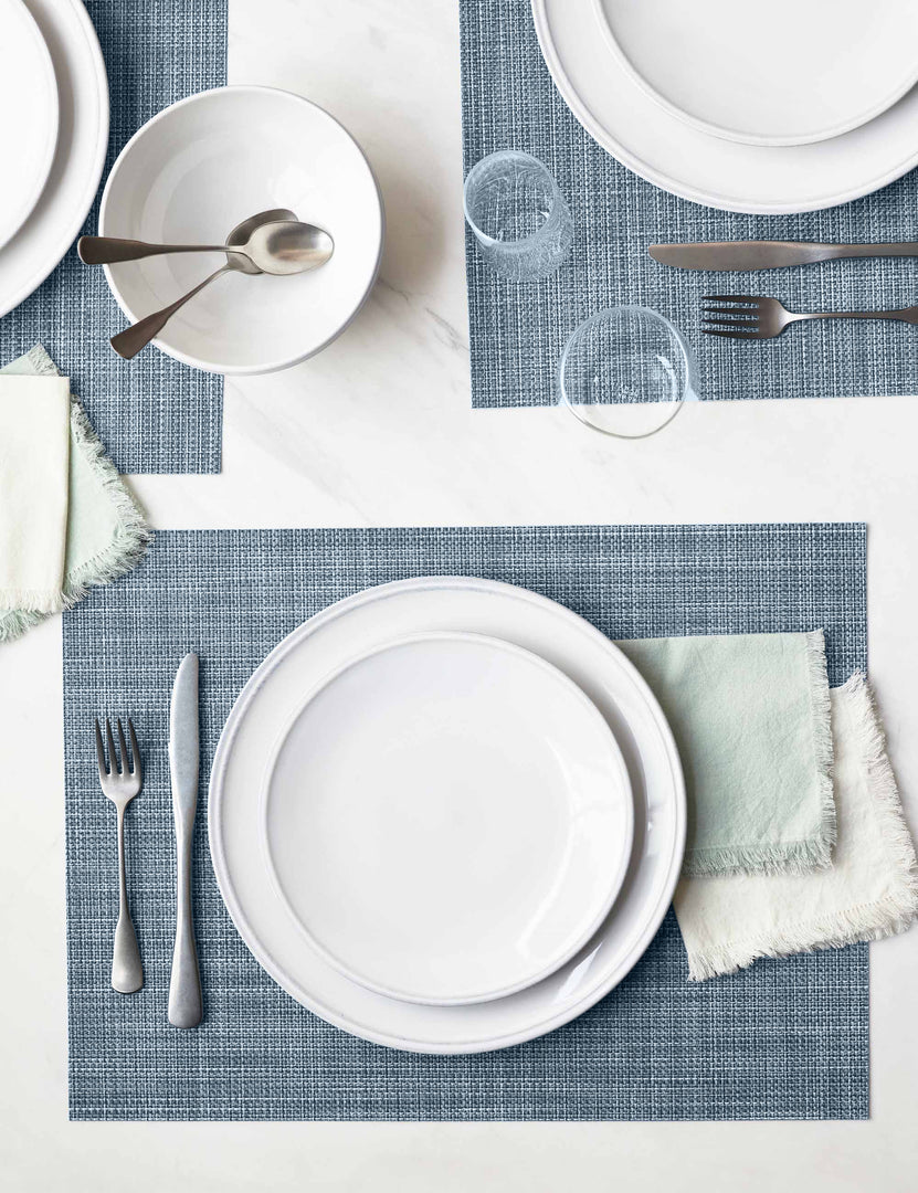 #color::chambray | The Set of four chambray blue Mini Basketweave Rectangle Placemat by Chilewich sits under a white dinnerware set