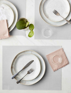 The Set of four sandstone gray Mini Basketweave Rectangle Placemat by Chilewich sits under a white dinnerware set