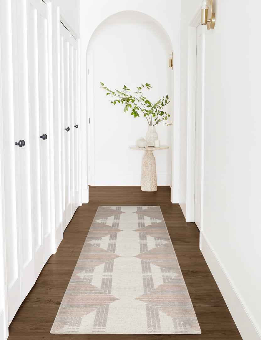#size::2-6--x-8- #size::6--x-9- #size::8--x-10- #size::9--x-12- #size::10--x-14- #size::12--x-15- | The Colette Rug in its runner size lays in a white arched hallway with a natural side table at the end
