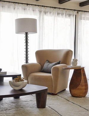 The Gem mango wood side table sits atop a plush ivory rug next to a beige velvet accent chair in a room with white curtains