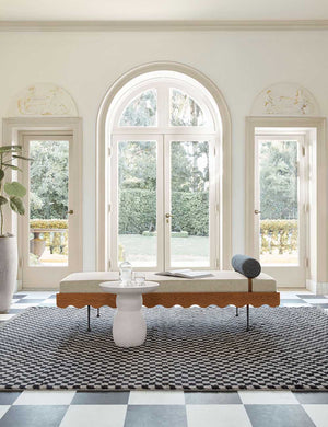 The Clouded White Round Side Table sits in front of a sculptural daybed on a black and white checkerboard carpet