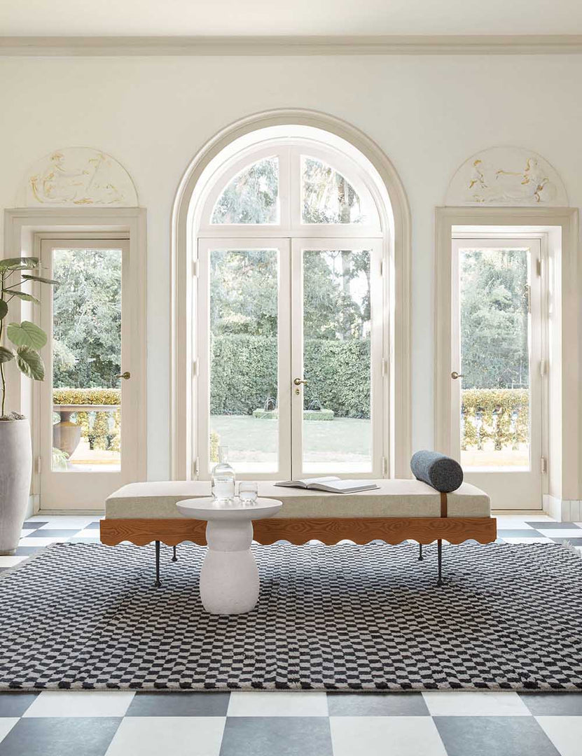 | The Clouded White Round Side Table sits in front of a sculptural daybed on a black and white checkerboard carpet