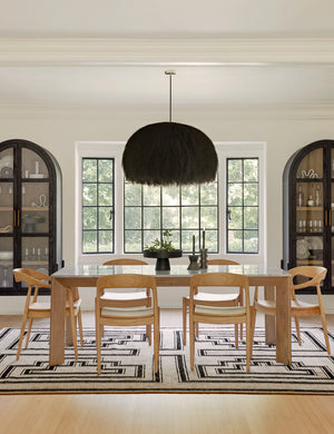 The Paige black plush pendant light with palm tree fibers sits in a symmetrical dining room with two tall wooden sideboards, a black and beige geometric rug, and natural wooden furniture