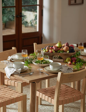 The set of six sand-toned stoneware nature dinner plates by thomas for rosenthal sit atop a wooden dining table in a dining room with woven chairs and an elevated wooden center piece