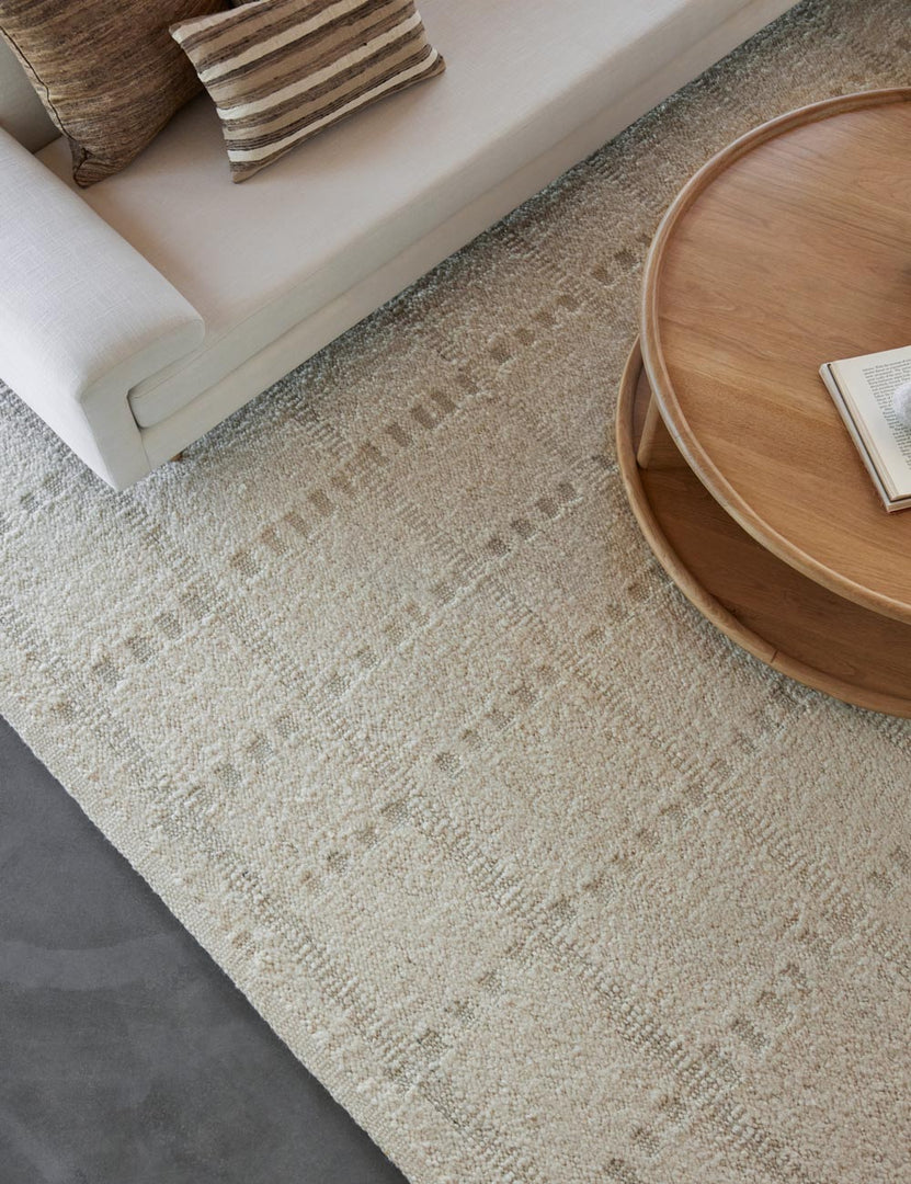 #size::2-6--x-8- #size::6--x-9- #size::8--x-10- #size::9--x-12- #size::10--x-14- #size::12--x-15- | Dolan wool ivory rug with a subtle hashed motif pattern lays under a circular wooden coffee table and ivory sofa