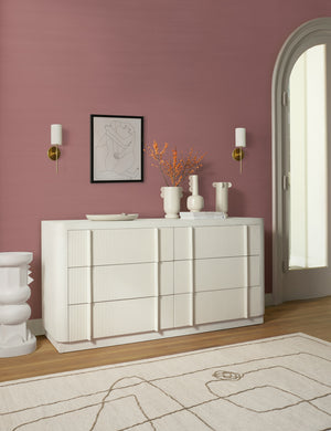 The Line Drawing Flatweave Rug lays in a room with dusty pink walls, a white sideboard, and a sculptural pedestal