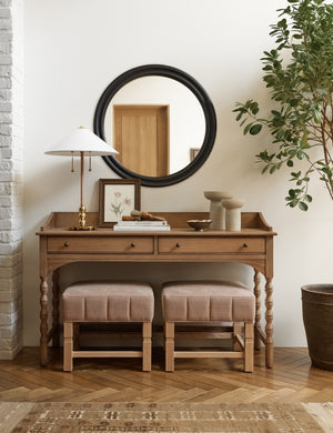 The Bourdon Double-Framed Black Round Mirror hangs on a cream wall above a mid-century wooden desk with two ottomans