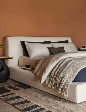 The Goleta gray chunky wool knit throw blanket with tasseled ends lays a linen framed bed in a bedroom with navy linens