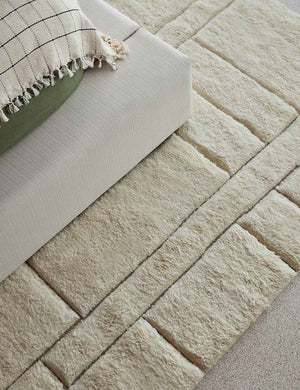 The Maleena cream hand-knotted wool and cotton area rug with abstract line tufting sits under a linen upholstered platform bedframe.