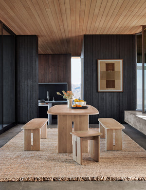 The Hagan rug lays under a rectangular wooden dining table, tow dining benches, and two dining stools
