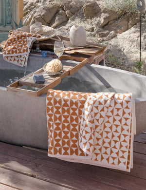 The Harper orange and white towel by house number 23 with half-moon designs is hung on a stone bathtub in an outdoor space