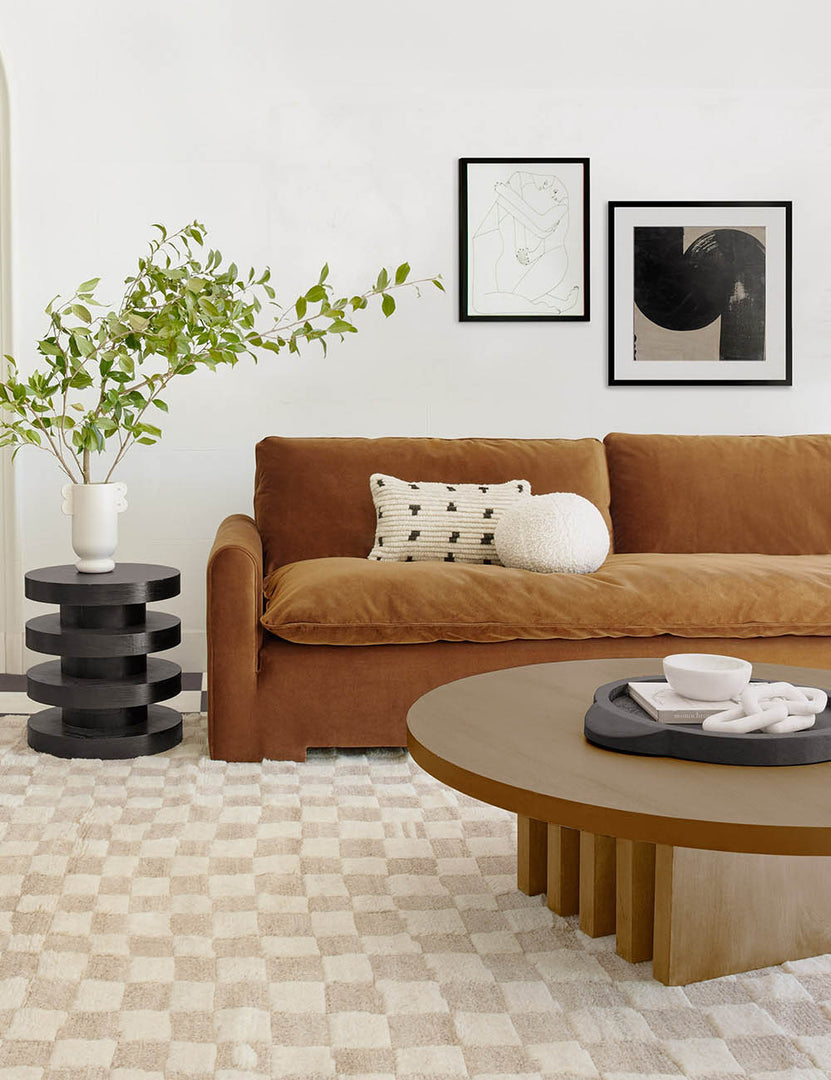 #color::natural | Pentwater natural wooden Round Coffee Table sits atop a white and natural checkered rug in front of a cognac velvet sofa