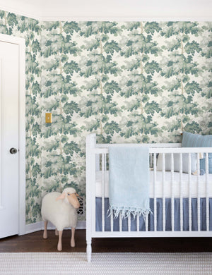 The Scalamandre botanical inspired green raphael wallpaper is in a nursery with a white crib and a toy lamb