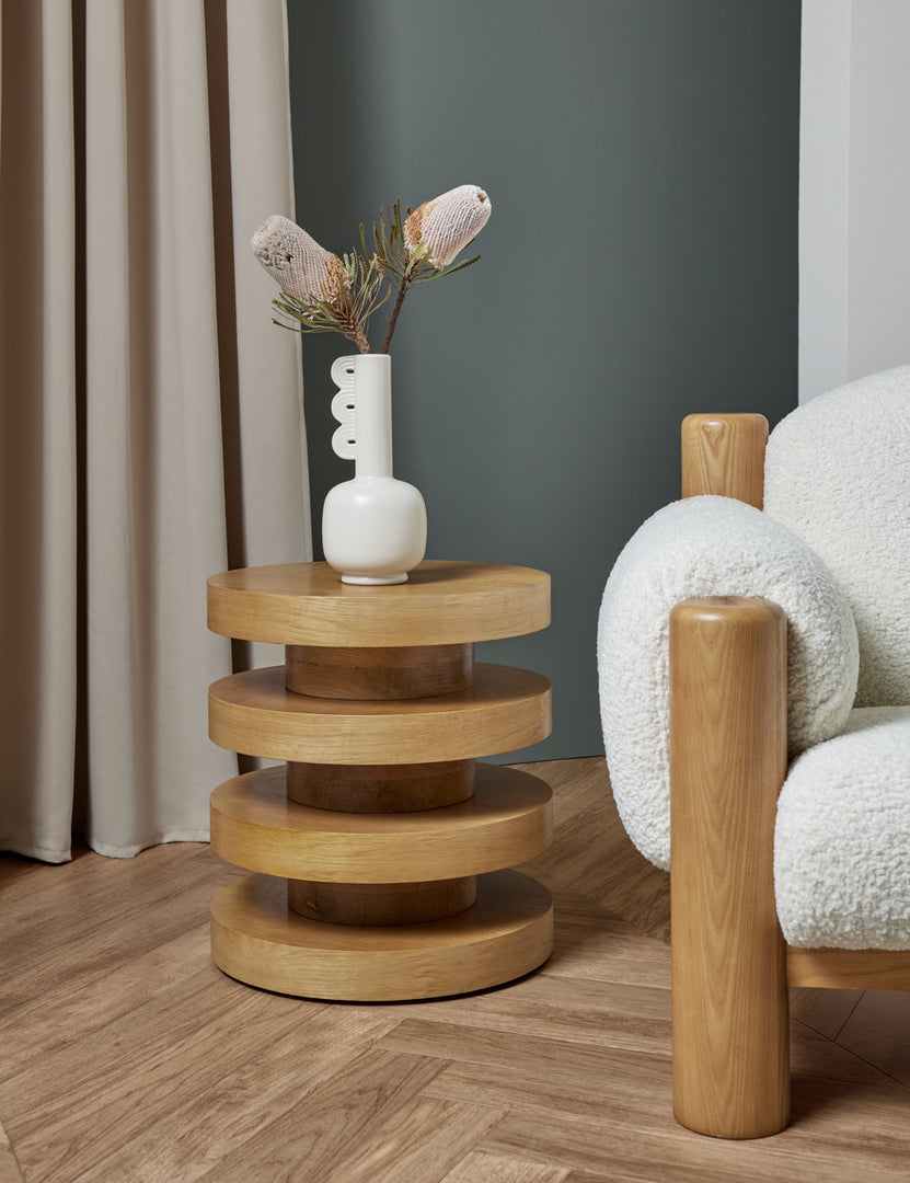 #color::natural | The Pentwater Four-Tiered Natural Round Side Table sits next to a boucle accent chair with a sculptural white vase