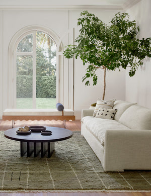 Irregular Dots Ivory Lumbar Pillow by Sarah Sherman Samuel sits on a linen couch in a living room with a round black coffee table and olive carpet