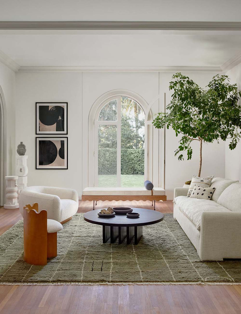 #color::black | Pentwater black wooden Round Coffee Table sits atop an olive green patterned rug between a linen sofa and two accent chairs