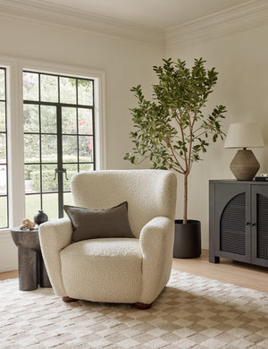 The Avery Boucle Cream accent chair sits atop a natural and beige checkerboard rug next to a sculptural side table