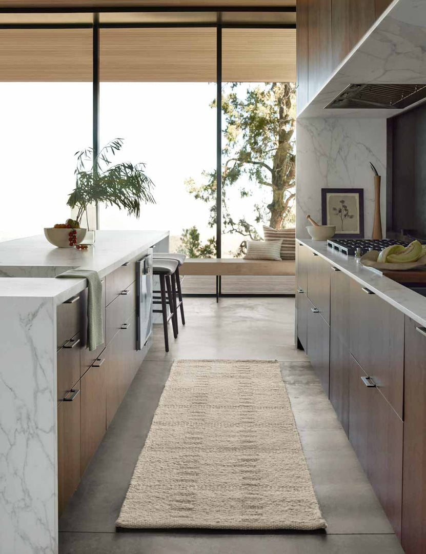 #size::2-6--x-8- | Dolan wool ivory rug in its runner size lays in a kitchen with wooden cabinetry and white marble countertops