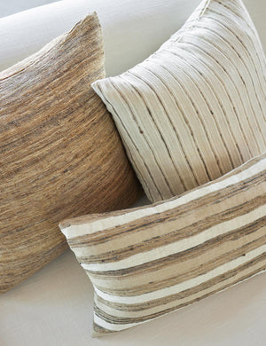 The Thora silk earth-toned striped lumbar pillow sits together with two other throw pillows on an ivory linen sofa