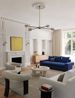 The Celeste black wood accent chair with wishbone frame sits in a bright living room with a white circular coffee table, navy blue sofa, and a black and white gridded rug.