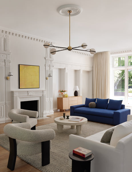 #color::black | The Celeste black wood accent chair with wishbone frame sits in a bright living room with a white circular coffee table, navy blue sofa, and a black and white gridded rug.