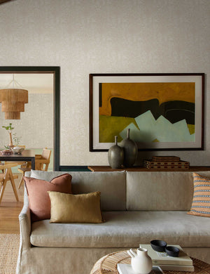 The Ema light gray vases with narrow necks and a marbled glaze sit in a living room atop a wooden sideboard with a gray linen couch and jute coffee table in front of it