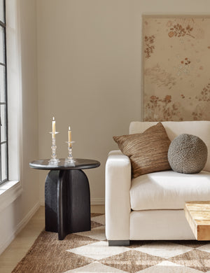 Khaki gray Bouclé Ball Pillow by Sarah Sherman Samuel sits on an ivory couch next to a black side table and atop a patterned rug