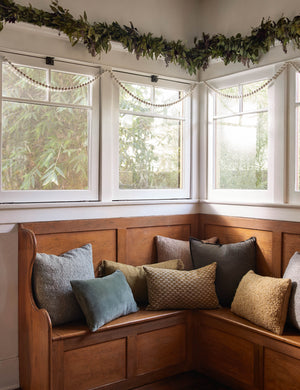 Manon linen boucle pillows sit on a wooden bench in a festive nook with a wooden bead garland and an olive garland hanging from the walls