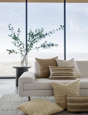 Jonas natural-toned Silk Pillow sits on a white sofa with other natural-toned throw pillows in a room with floor to ceiling windows