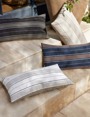 The whitehaven indoor and outdoor pillow lays on a stone staircase outside with the other colors of the whitehaven pillow