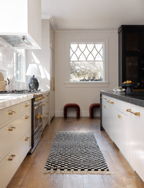 #size::2-6--x-8- | Black and white Checkerboard Rug by Sarah Sherman Samuel in its runner size lays in a kitchen with marble counter tops and golden hardware