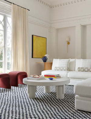 The Anja white indoor and outdoor round coffee table sits atop a black and white checkerboard rug next to a white sectional