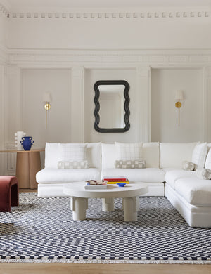 Black and white Checkerboard Rug by Sarah Sherman Samuel lays in a living room with a round sculptural coffee table and rounded sofa