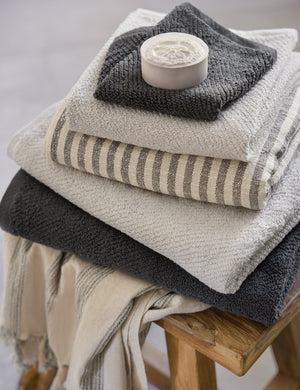 The midnight gray turkish cotton Air Weight Towel Set by Coyuchi sits in a stack amongst other bathroom towels atop a wooden stool