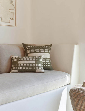 The Stonewalk green geometric throw pillow by Élan Byrd sits on a natural linen cushioned bench next to a jute basket