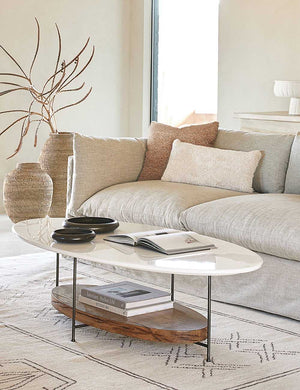 The Manon linen terracotta orange square boucle pillow sits on a gray linen sofa in a living room with the thomas bina oval coffee table