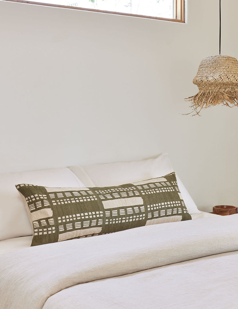 #size::14--x-40- | Stonewalk green geometric long lumbar throw pillow by Élan Byrd lays on a bed with natural toned linens to the left of a jute pendant light