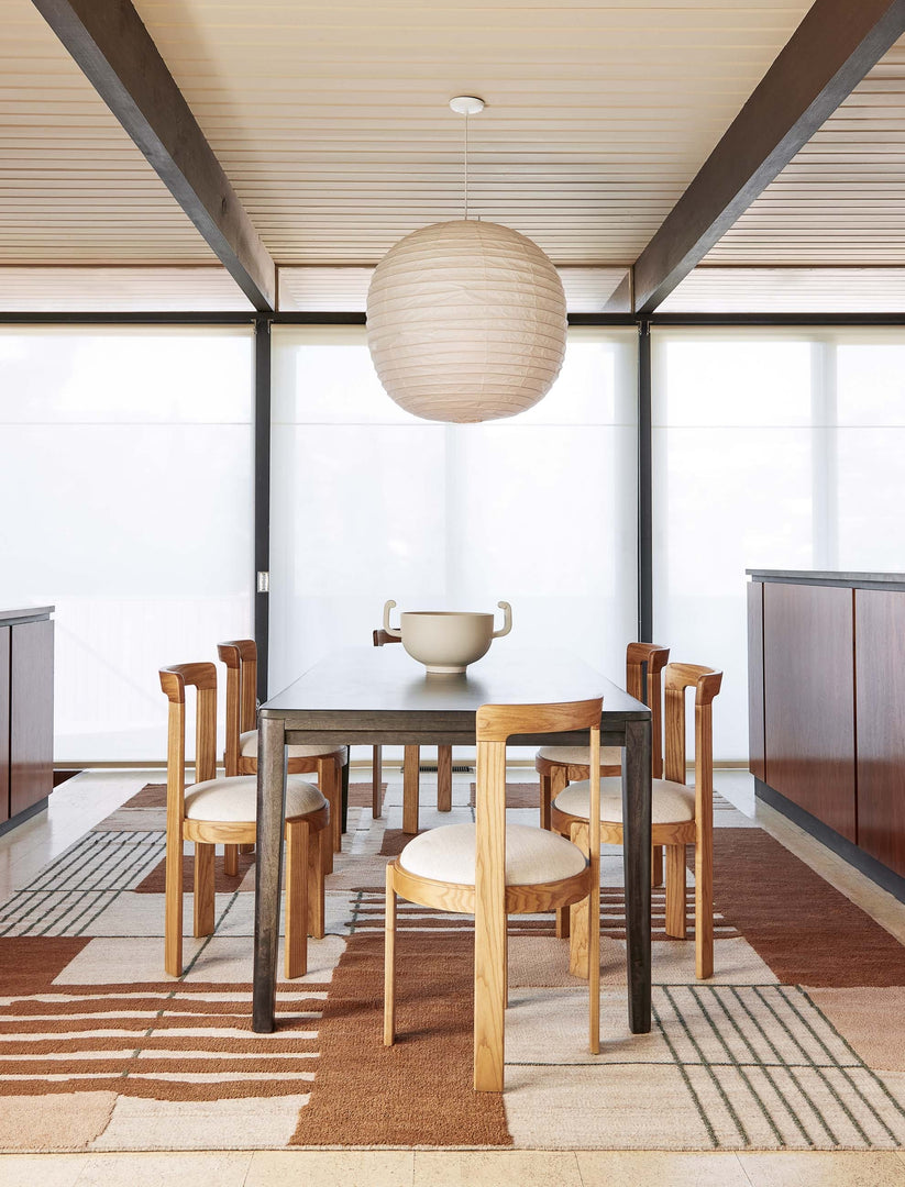 #size::2--x-3- #size::2-6--x-8- #size::5--x-8- #size::6--x-9- #size::8--x-10- #size::9--x-12- #size::10--x-14- #size::12--x-15- | The Benita natural toned hand-knotted floor rug by Nina Freudenberger lays in a dining room with a black wooden dining table, sculptural dining chairs, and a white centerpiece bowl